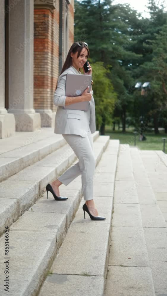 Vertical shot of a business woman in a suit talking on the phone and walking down the stairs outside the office building. Vertical shot of a business woman in a suit talking on the phone and walking down the stairs outside the office building.