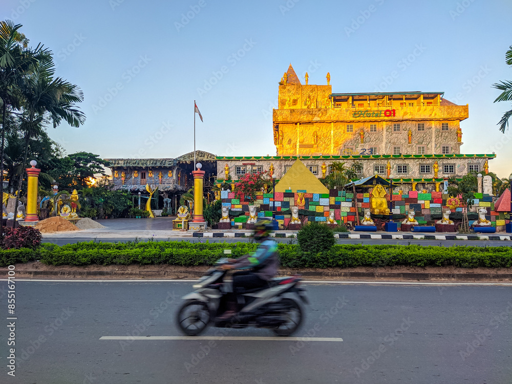 Unique castle-like hotel in Batam city, adorned with colorful decorations and a small pyramid at its base, standing prominently on a street corner under a clear blue sky