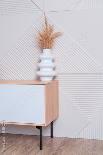 A ceramic white vase with a dry plant on a low bedside table. An interior design detail.