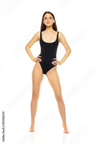 Young brunette woman in one piece bikini swimsuit posing on a whitestudio background. Front view.