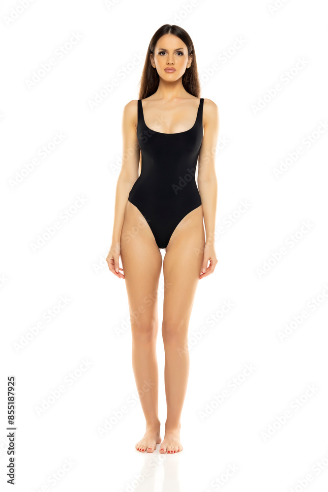 Young brunette woman in one piece bikini swimsuit posing on a whitestudio background. Front view. Young brunette woman in one piece bikini swimsuit posing on a whitestudio background. Front view.