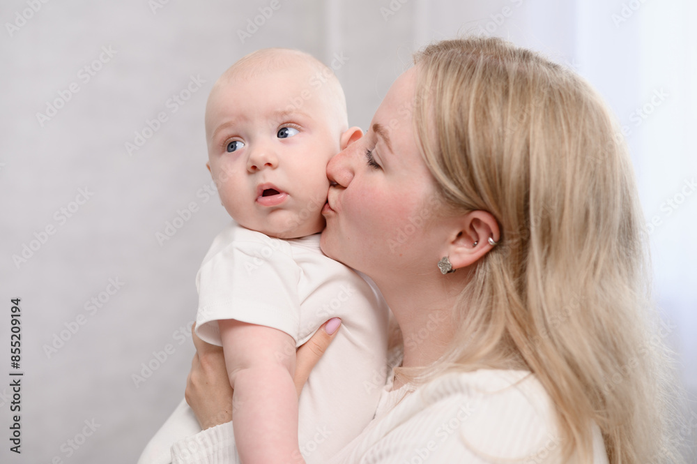 Woman mom gently kisses her newborn baby on cheek while holding him in her arms, showing heartfelt gesture of love and tenderness. Concept of motherhood, maternity leave, infancy Woman mom gently kisses her newborn baby on cheek while holding him in her arms, showing heartfelt gesture of love and tenderness. Concept of motherhood, maternity leave, infancy
