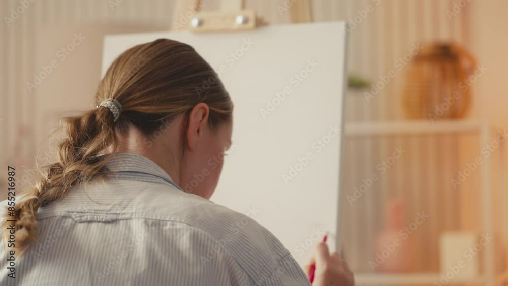 Focused woman artist making a sketch, preparing to paint on easel stand Focused woman artist making a sketch, preparing to paint on easel stand