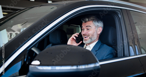 Caucasian businessman talking on phone, touching steering wheel and looking around inside automobile. Successful man buy vehicle in car dealership. Portrait of a businessman in a car with a phone.