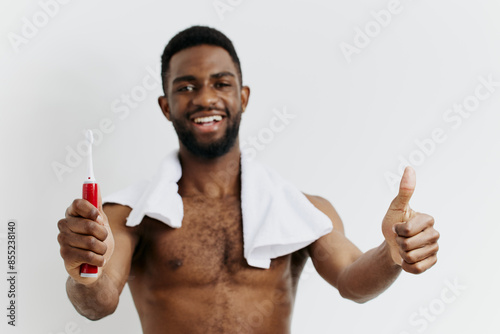 Confident shirtless black man holding toothbrush and giving thumbs up to promote dental hygiene and selfcare photo