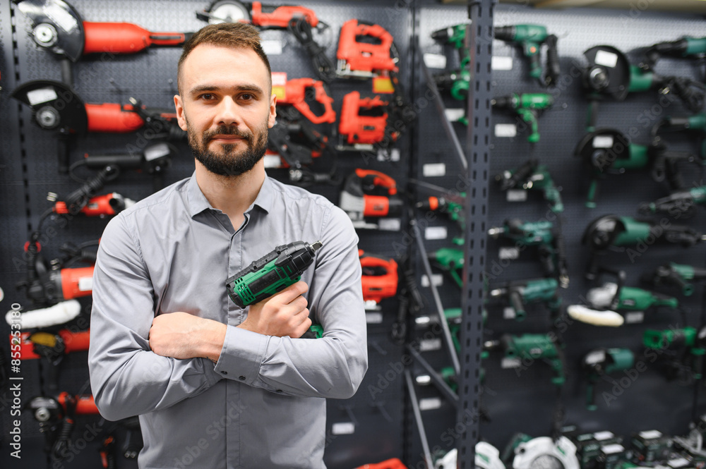 a man in a hardware store chooses a new screwdriver next to a showcase of power tools a man in a hardware store chooses a new screwdriver next to a showcase of power tools