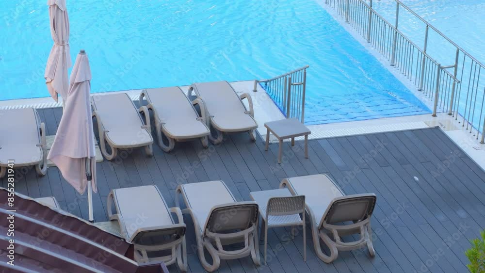 Empty lounge chairs and tables by a blue pool in 4k slow motion 60fps Empty lounge chairs and tables by a blue pool in 4k slow motion 60fps