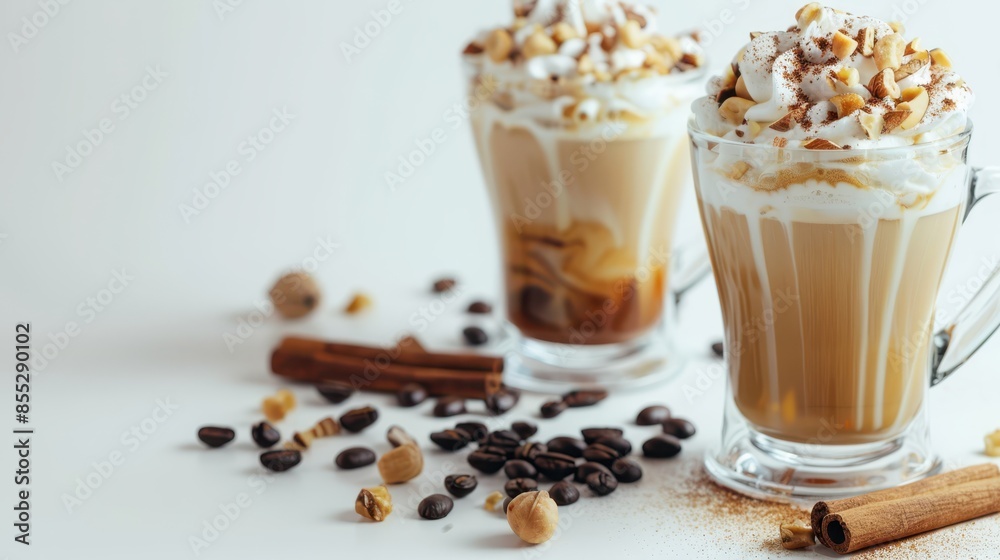 Two glasses of layered coffee topped with whipped cream, nuts, and cinnamon, surrounded by coffee beans and cinnamon sticks on a white background. Delicious fall beverage concept. Two glasses of layered coffee topped with whipped cream, nuts, and cinnamon, surrounded by coffee beans and cinnamon sticks on a white background. Delicious fall beverage concept.