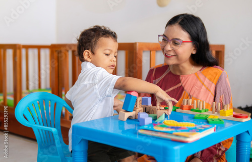 Single Latina mother watches her child interact and play with wooden blocks of different colors used in therapy and child development