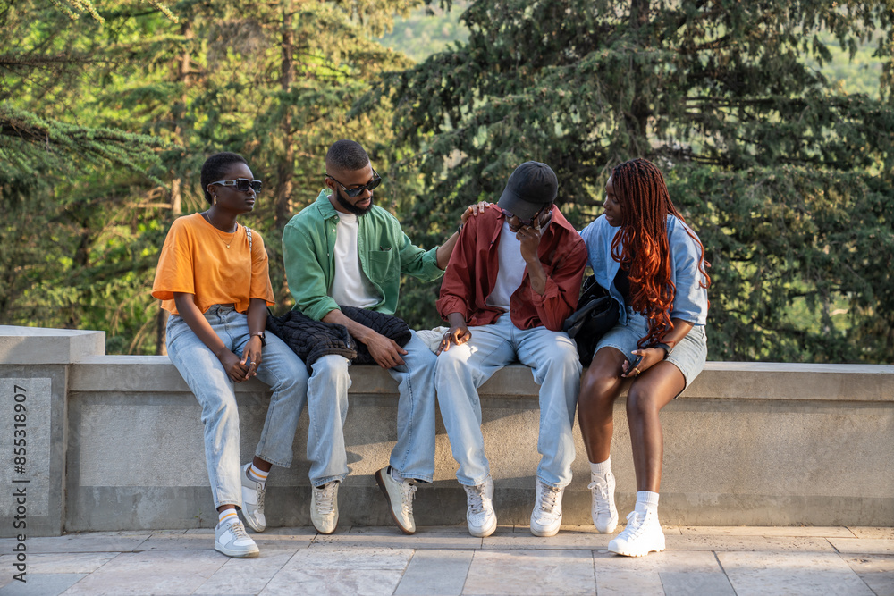 Fototapeta premium Group of African friends together outside. Company of black students provide friendly support to upset guy. Classmates listen to buddy experiencing problems with studies and romantic relationships. 