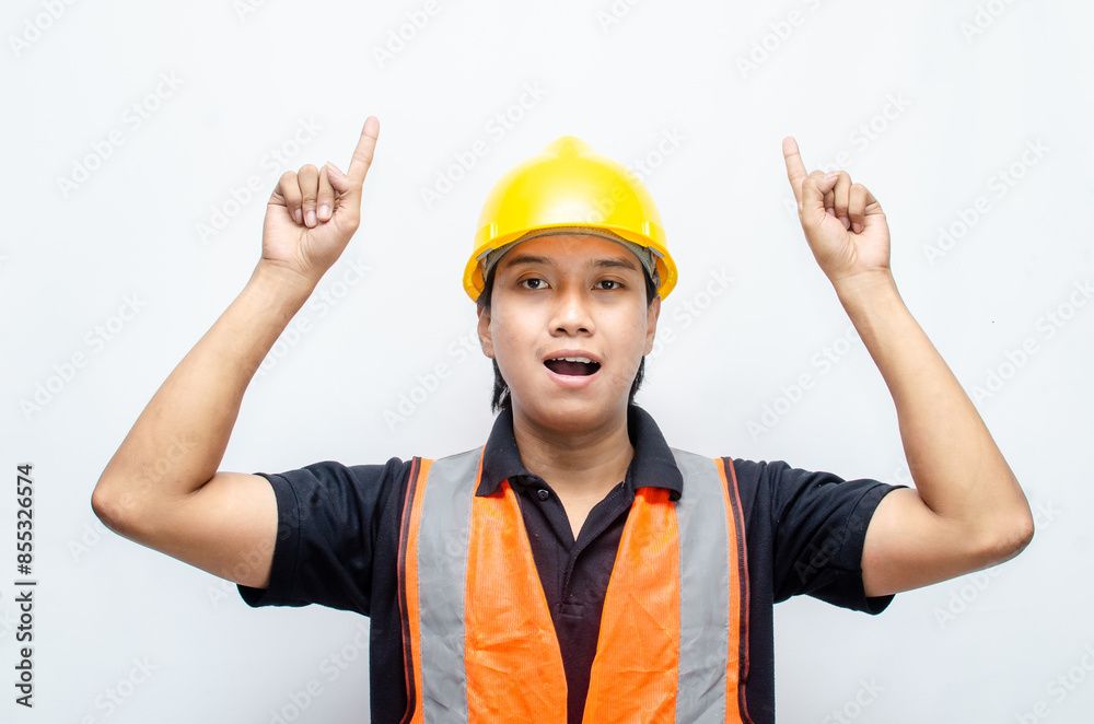 A happy, surprised asian construction worker in black shirt and yellow safety helmet pointing a finger and presenting something ads.	
