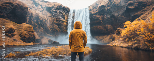 A person in a yellow jacket is mesmerized by a majestic waterfall surrounded by autumn colors photo