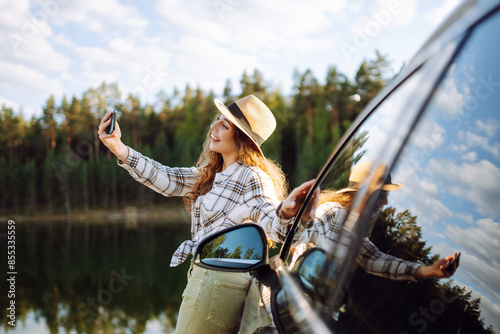 Young female tourist traveling by car taking selfie. Rest stop in car trip to take photos. Active lifestyle, blogging, nature, weekend.
