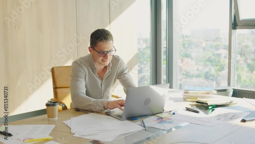 A professional entrepreneur works focused on tasks in a modern office setting. Bright workspace with a busy atmosphere, laptop and documents on desk, showing determination and productivity