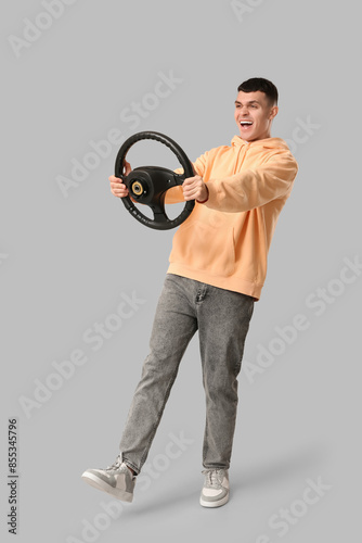 Emotional young man with steering wheel on grey background