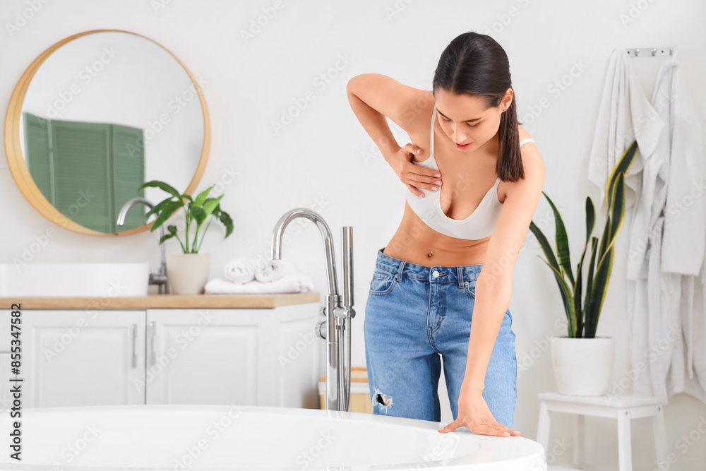 Young woman suffering from breast pain in bathroom. Cancer awareness concept Young woman suffering from breast pain in bathroom. Cancer awareness concept