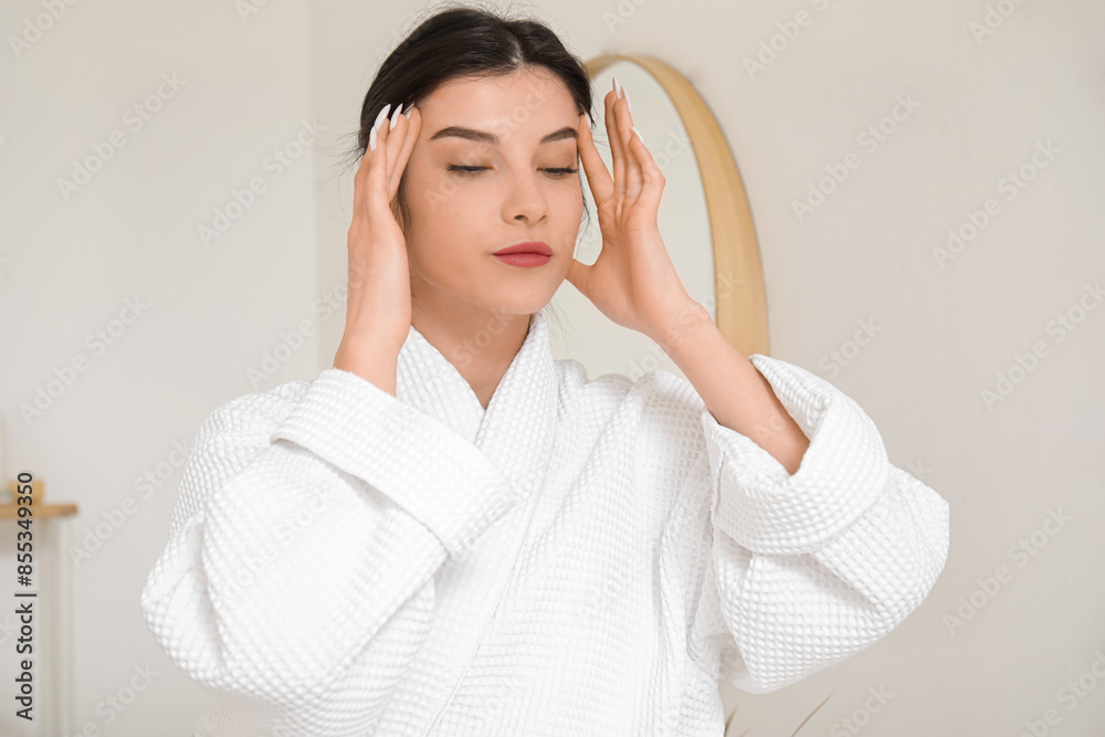 Beautiful young woman in bathrobe doing face building exercise at home Beautiful young woman in bathrobe doing face building exercise at home