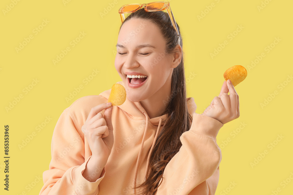 Young woman eating potato chips on yellow background, closeup Young woman eating potato chips on yellow background, closeup