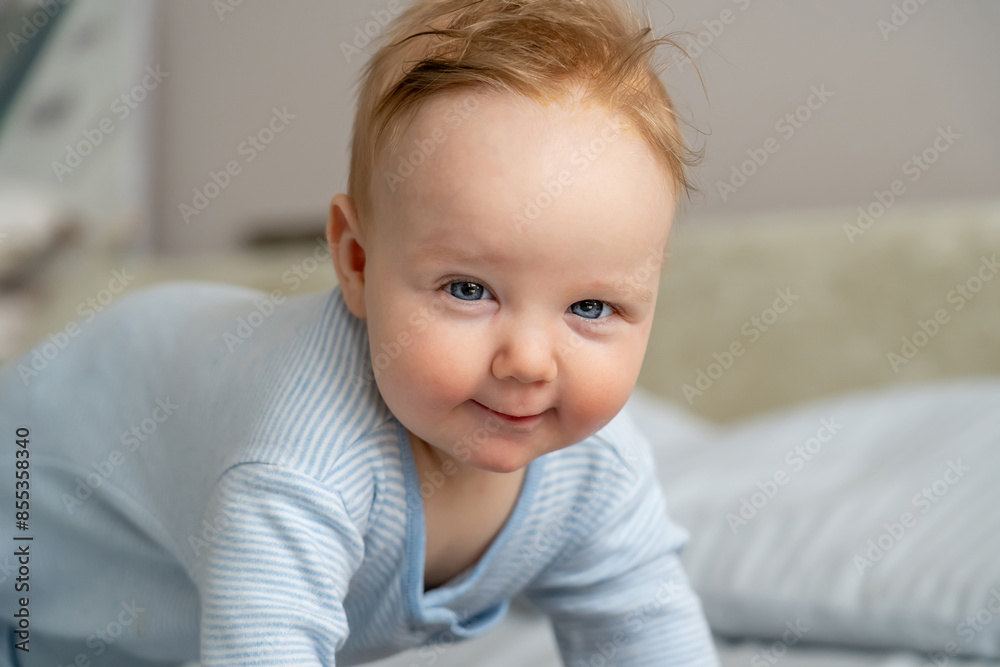 A close-up photo of a smiling baby girl in a blue onesie, crawling on a bed at home A close-up photo of a smiling baby girl in a blue onesie, crawling on a bed at home