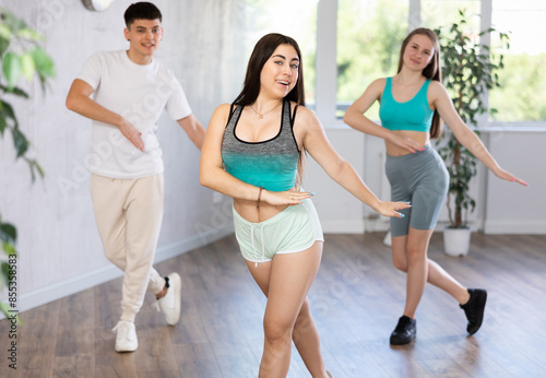 Portrait of positive teenager learning dynamic dance moves with group of teens in modern studio