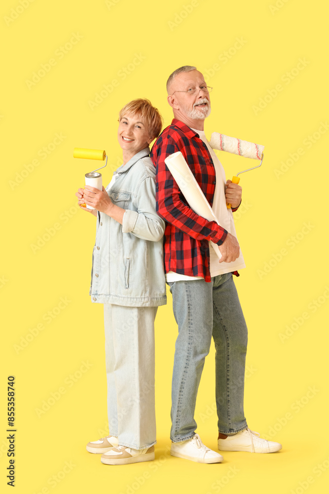 Mature couple with paint cans and rollers on yellow background Mature couple with paint cans and rollers on yellow background