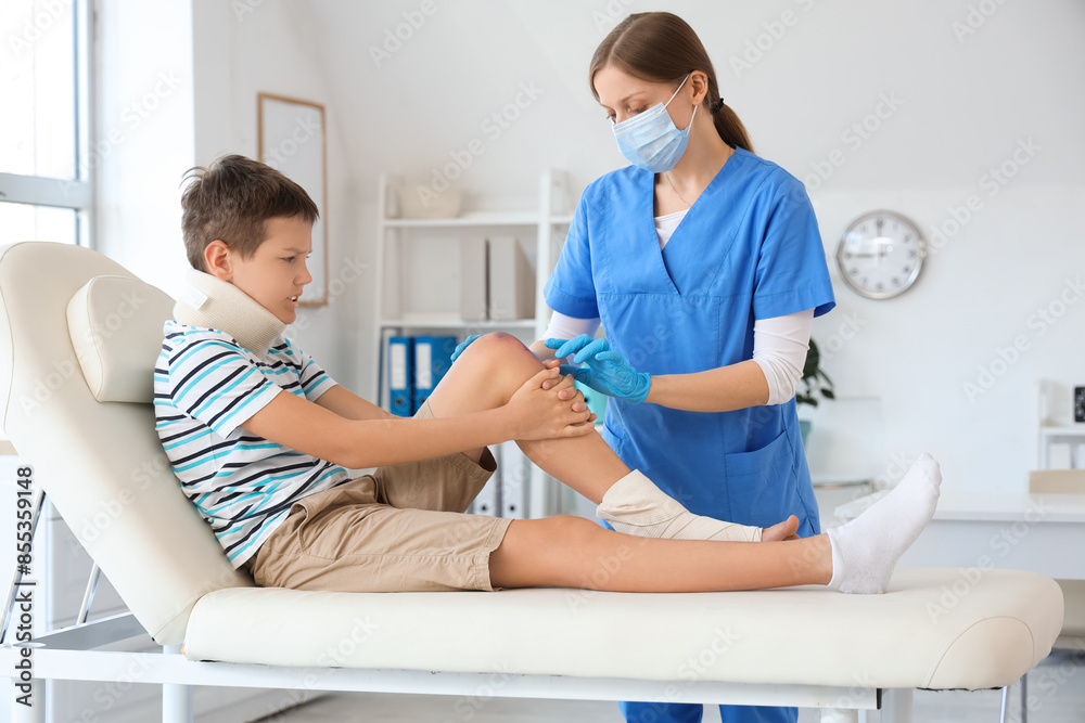 Fototapeta premium Injured little boy with bruised knee visiting doctor in clinic
