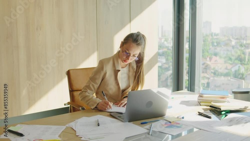 A dedicated businesswoman focused on work in a modern office, with a laptop and documents. She is efficient, organized, and productive, showcasing strong leadership and professional skills