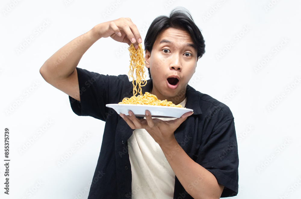 young asian man barehanded pinching fried instant noodles into his mouth. attractive asian man demonstrating how tasty the noodles are. young asian man barehanded pinching fried instant noodles into his mouth. attractive asian man demonstrating how tasty the noodles are.