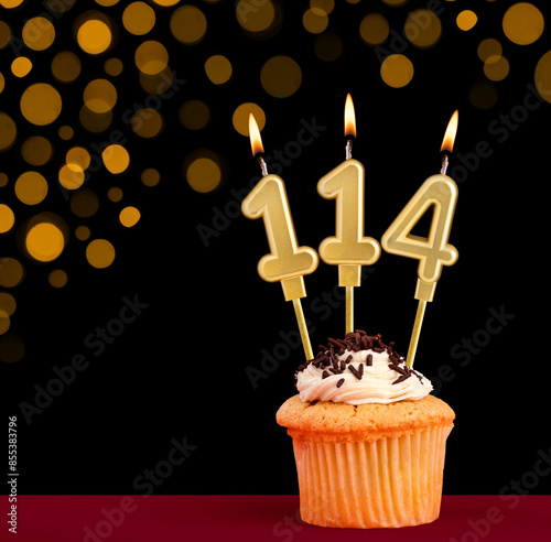 Number 114 birthday candle - Cupcake on black background with out of focus lights photo