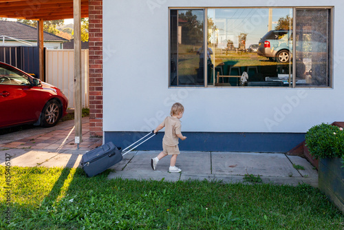 Toddler boy helping family carry suitcase of luggage inside at holiday house destination photo