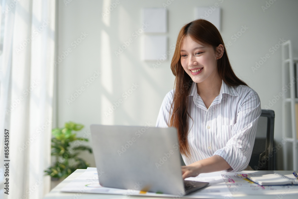 Smiling businesswoman working on laptop in a bright office, enjoying a productive workday, seated at a desk with documents and coffee. Smiling businesswoman working on laptop in a bright office, enjoying a productive workday, seated at a desk with documents and coffee.