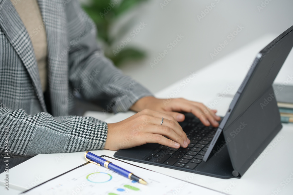 Close-up of a professional working on a tablet with a keyboard cover, analyzing charts and data at a desk. Close-up of a professional working on a tablet with a keyboard cover, analyzing charts and data at a desk.