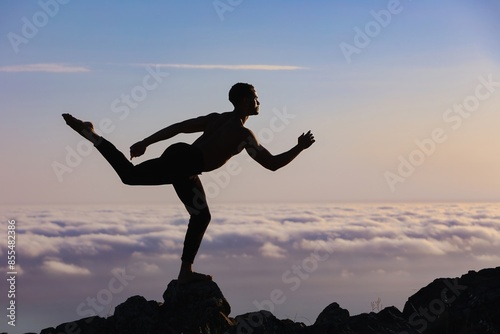 Silhouette of male ballet dancer posing a majestic dance move on rocks. Behind him are heavenly clouds at sunset.