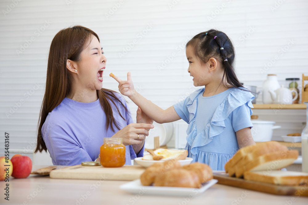 mother tasting orange jam with her daughter in the kitchen mother tasting orange jam with her daughter in the kitchen