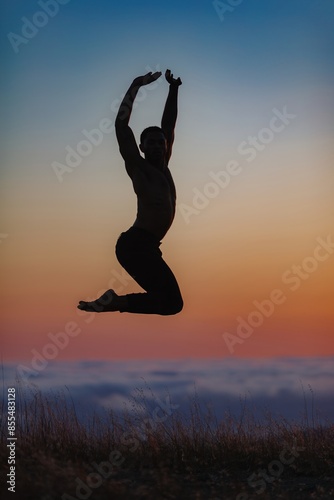 Silhouette of male ballet dancer jumping and doing a majestic dance move in nature, Behind him are heavenly clouds and the sun is setting. photo