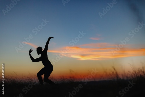 Silhouette of male ballet dancer doing a majestic dance move in nature, Behind him are heavenly clouds and the sun is setting. photo