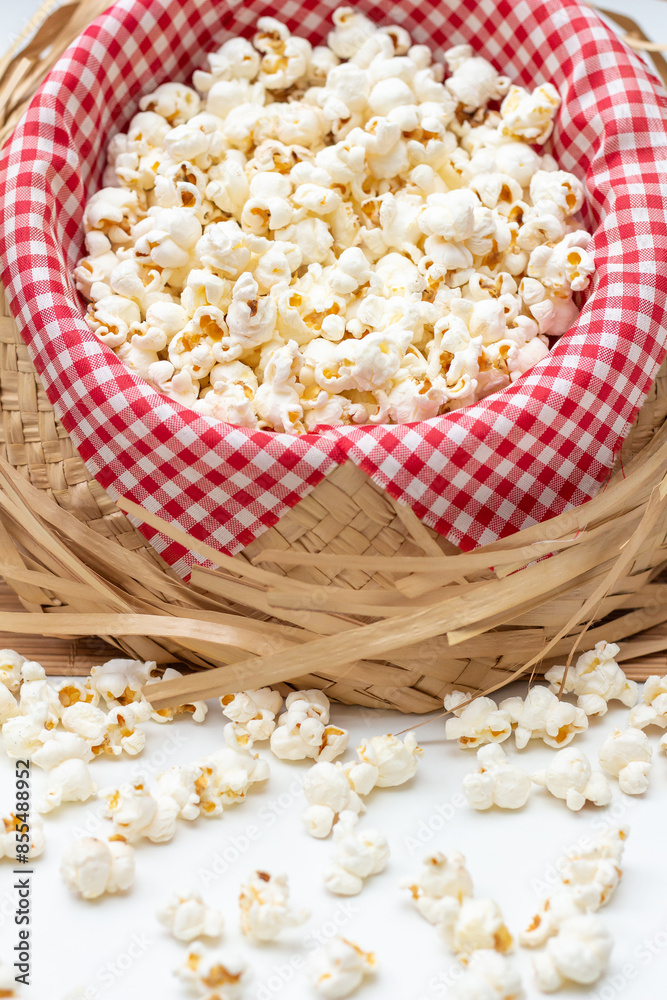 Front view of a tilted straw hat with red and white checkered fabric and salted popcorn inside. With loose popcorn scattered in front. Typical food for the São João June festival.