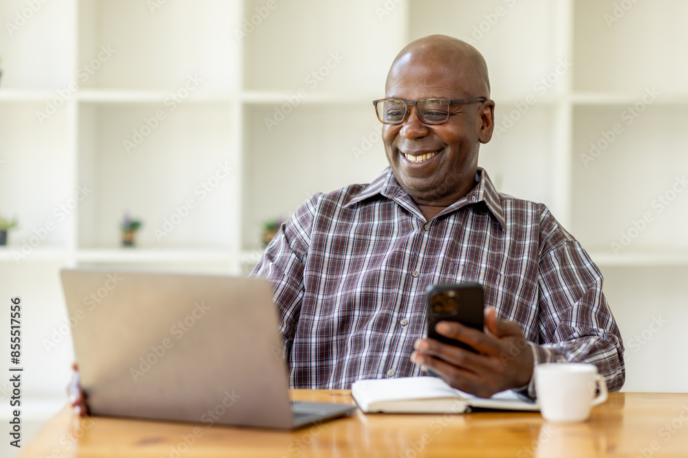 Portrait of happy smiling senior man sitting on desk at cafe using smartphone and laptop