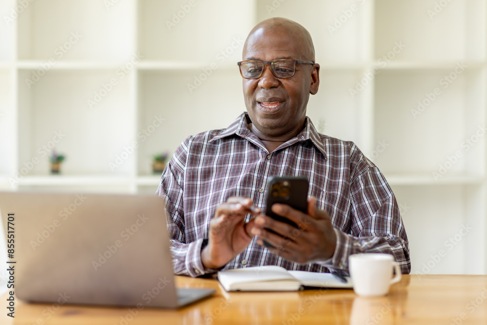 Portrait of happy smiling senior man sitting on desk at cafe using smartphone and laptop Portrait of happy smiling senior man sitting on desk at cafe using smartphone and laptop