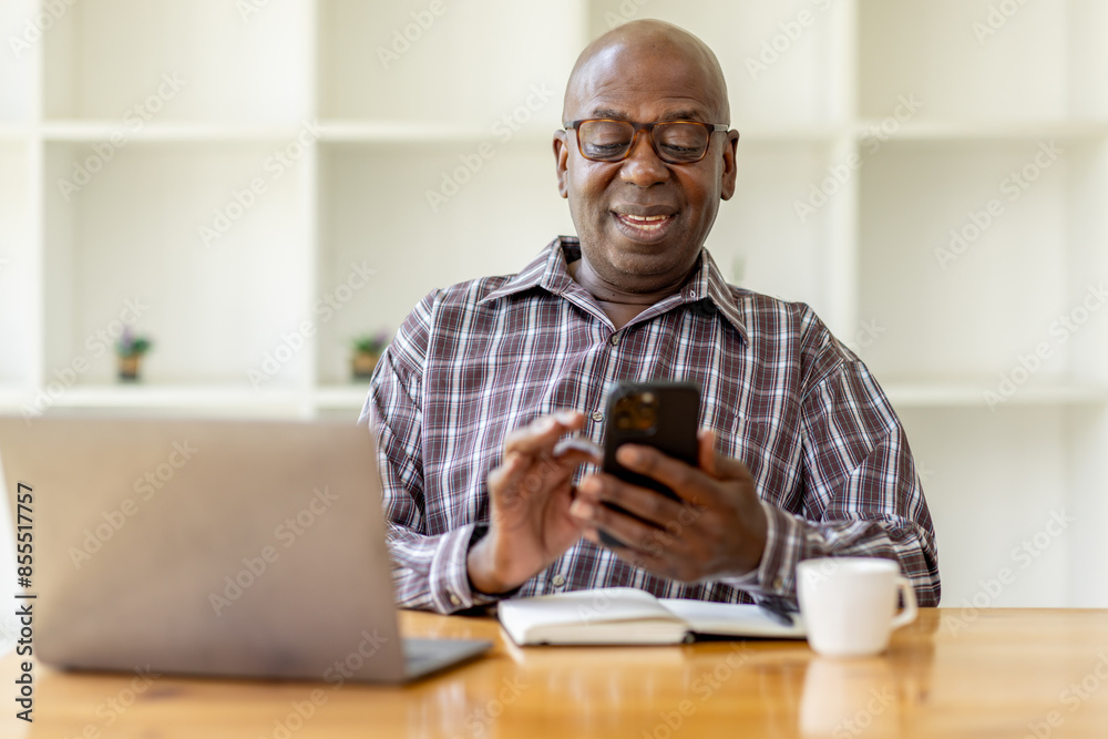 Portrait of happy smiling senior man sitting on desk at cafe using smartphone and laptop Portrait of happy smiling senior man sitting on desk at cafe using smartphone and laptop