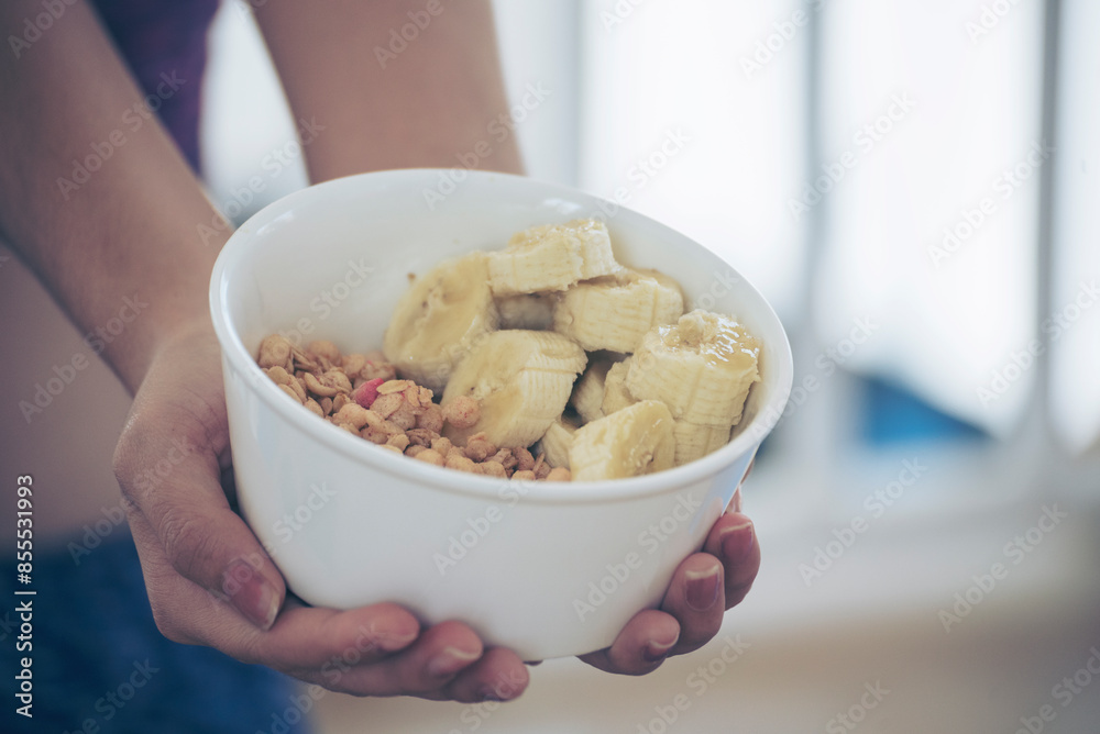 Asian women eating cereal oatmeal with milk organic nutrition ingredients. Women hands holding spoon and bowl with healthy dairy product cereal, fruits, banana. Dietary healthy lifestyle at home Asian women eating cereal oatmeal with milk organic nutrition ingredients. Women hands holding spoon and bowl with healthy dairy product cereal, fruits, banana. Dietary healthy lifestyle at home
