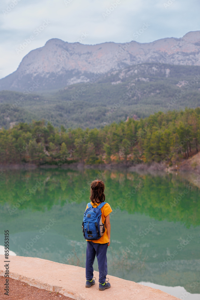 Naklejka premium summer camp. a boy with a backpack looks at a beautiful mountain lake. Relaxed, peaceful, thoughtful, happy and free child on a mountain lake.
