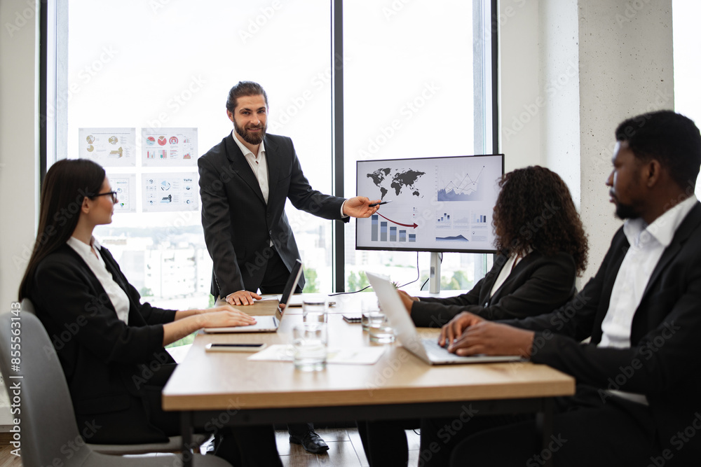 Businessman presenting to colleagues in modern meeting room. Group discussing data and statistics displayed on screen and charts. Professional team engaged in business discussion around table. Businessman presenting to colleagues in modern meeting room. Group discussing data and statistics displayed on screen and charts. Professional team engaged in business discussion around table.
