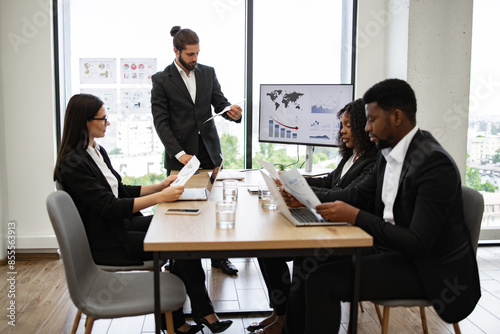 Group reviewing charts and graphs during presentation led by colleague. Team of professionals in business meeting discussing financial reports and data analysis.