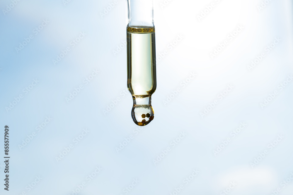 A drop of cosmetic aromatic oil drips from the pipette. Front view. A drop of cosmetic aromatic oil drips from the pipette. Front view.