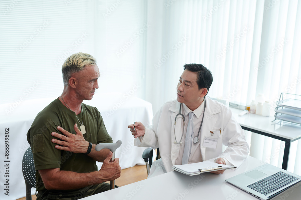 Obraz premium Soldier complaining on his injured arm to doctor during his visit to hospital
