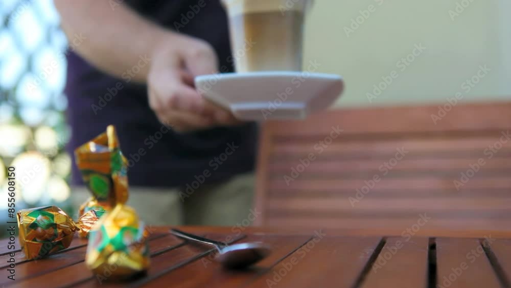 Male hand puts a glas with caffee late macchiato on a table 