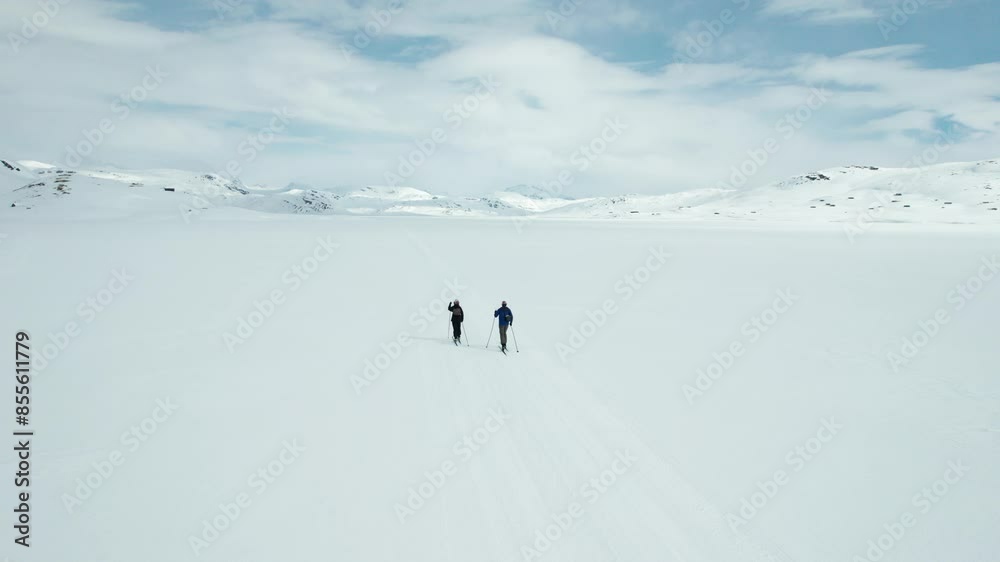 Two people are cross country skiing across a snowy landscape on a frozen lake in Tyin, Norway. Two people are cross country skiing across a snowy landscape on a frozen lake in Tyin, Norway.