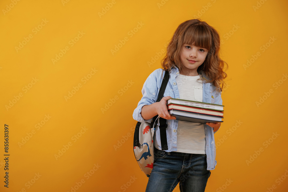 Holding books. Cute little girl is against yellow background Holding books. Cute little girl is against yellow background
