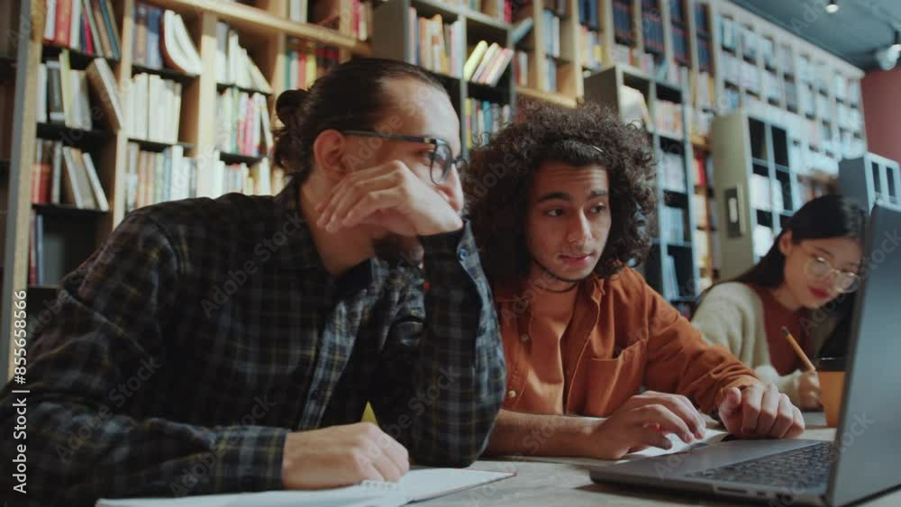 Young middle-eastern college student discussing homework on laptop with group mate at desk in public library
